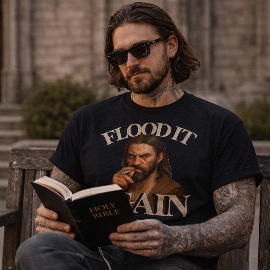 Man wearing a t-shirt with a graphic design, sitting on a bench reading a book.